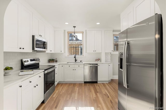 kitchen featuring appliances with stainless steel finishes, decorative light fixtures, white cabinetry, light hardwood / wood-style floors, and sink