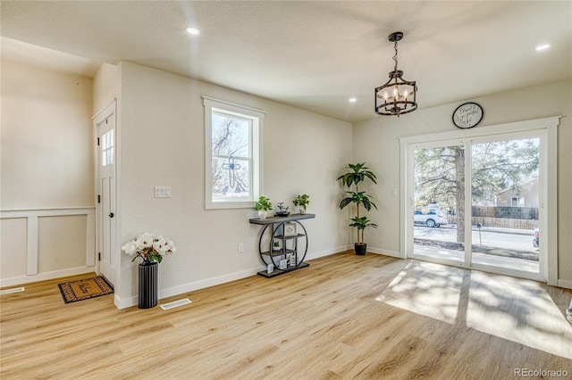 doorway to outside with a wealth of natural light, a notable chandelier, visible vents, and wood finished floors