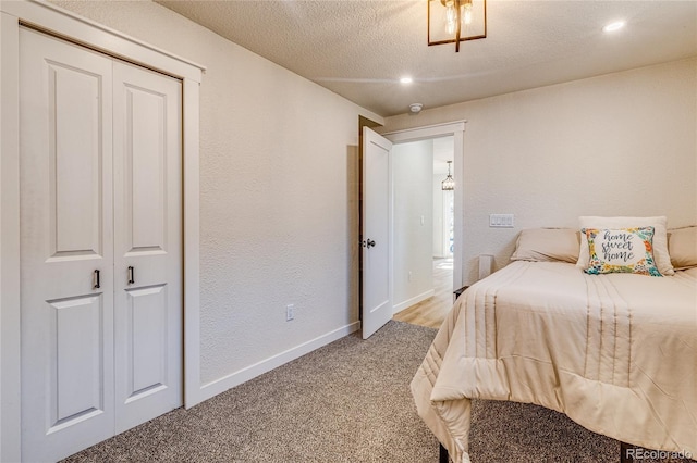 bedroom featuring light carpet, a textured ceiling, baseboards, and a textured wall