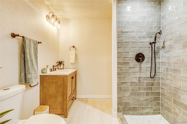 full bath featuring vanity, toilet, wood finished floors, and a tile shower