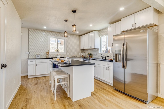 kitchen with dark countertops, stainless steel fridge, decorative backsplash, and white cabinets
