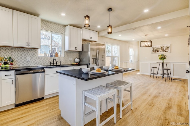 kitchen with a sink, a breakfast bar, white cabinets, dark countertops, and appliances with stainless steel finishes
