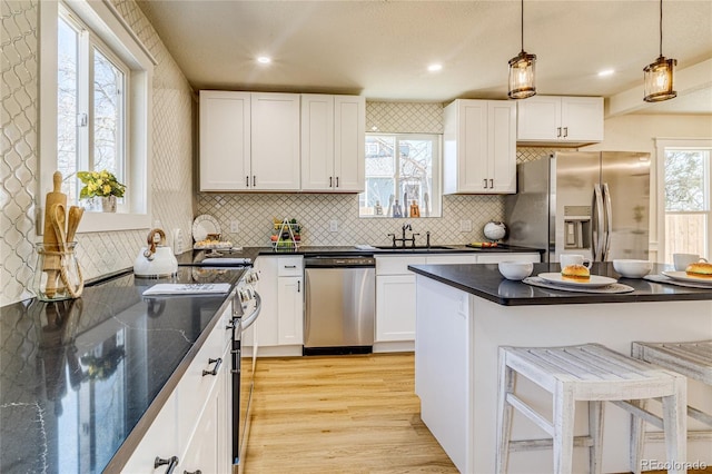 kitchen with light wood-type flooring, stainless steel appliances, a kitchen breakfast bar, and dark countertops