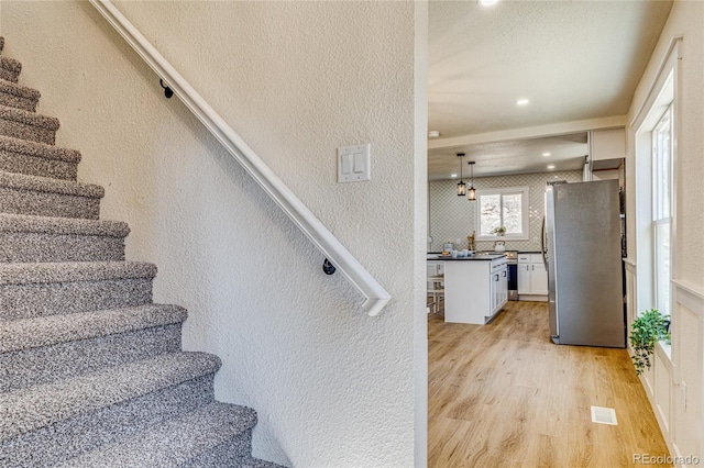 stairway featuring recessed lighting, visible vents, wood finished floors, and a textured wall