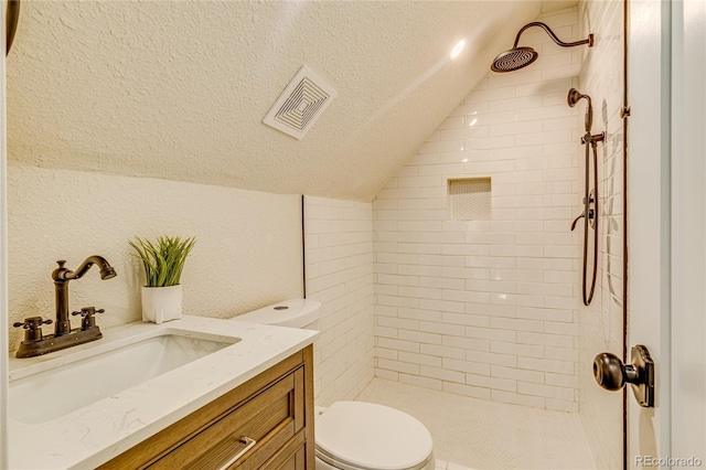 bathroom featuring toilet, a tile shower, a textured ceiling, visible vents, and lofted ceiling