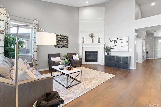 living area with dark wood-type flooring, a glass covered fireplace, baseboards, and a high ceiling