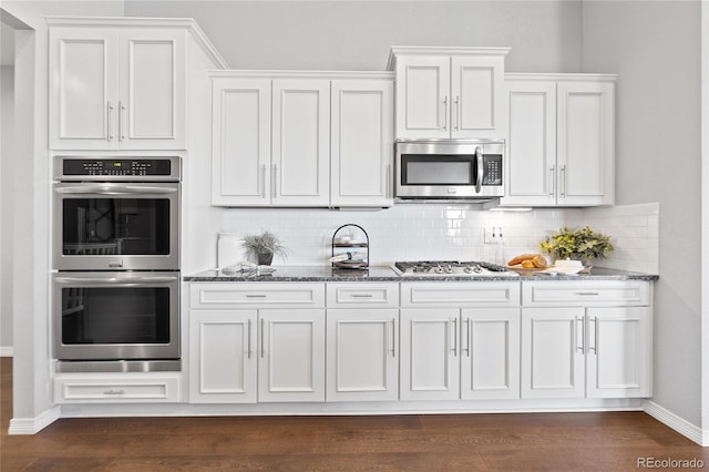 kitchen featuring appliances with stainless steel finishes, white cabinetry, backsplash, and dark stone countertops