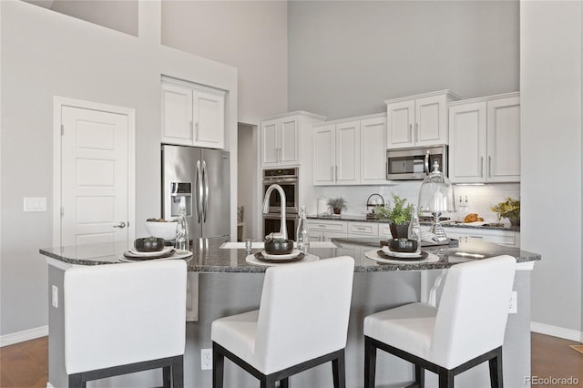 kitchen with stainless steel appliances, dark wood-type flooring, a towering ceiling, white cabinets, and backsplash