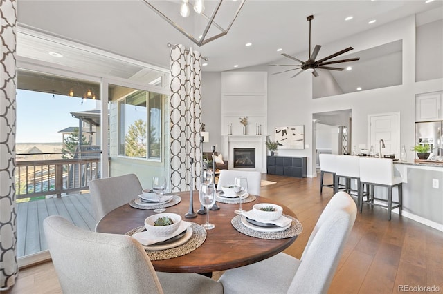 dining area with a ceiling fan, a glass covered fireplace, wood finished floors, high vaulted ceiling, and recessed lighting