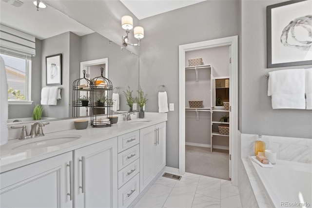 full bathroom featuring double vanity, a relaxing tiled tub, a sink, and a walk in closet