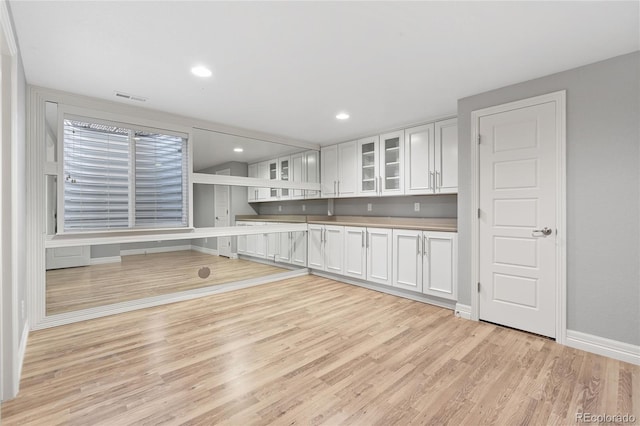 kitchen with baseboards, visible vents, white cabinets, glass insert cabinets, and light wood-type flooring