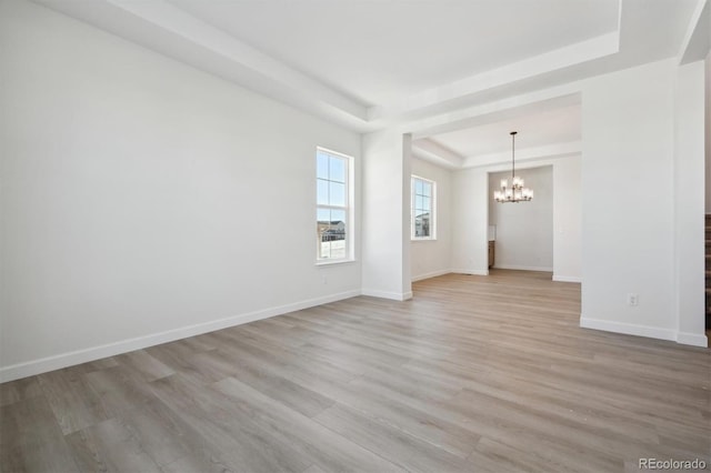 empty room featuring a chandelier, light wood-type flooring, and a tray ceiling