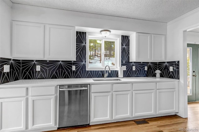 kitchen featuring light wood finished floors, white cabinetry, a sink, decorative backsplash, and stainless steel dishwasher