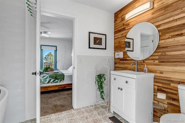 bathroom with wooden walls, ensuite bath, vanity, and a textured ceiling