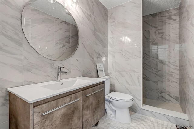 full bath with toilet, vanity, tiled shower, a textured ceiling, and tile walls