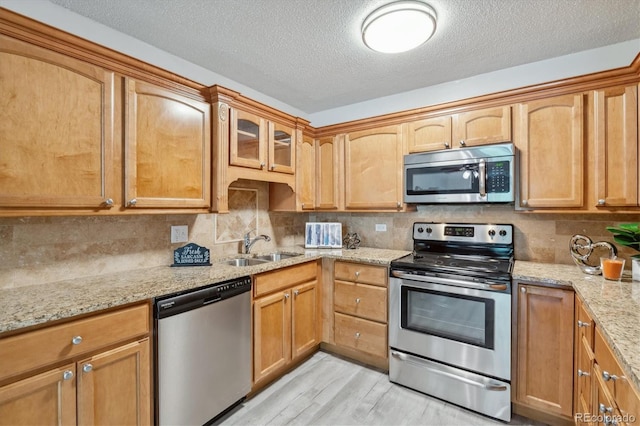 kitchen featuring stainless steel appliances, sink, backsplash, light stone counters, and light hardwood / wood-style flooring