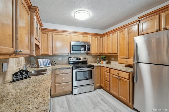 kitchen with light wood-type flooring, appliances with stainless steel finishes, backsplash, and light stone countertops