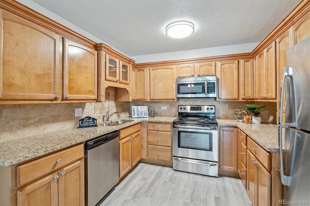 kitchen with stainless steel appliances, decorative backsplash, sink, light stone counters, and light hardwood / wood-style flooring