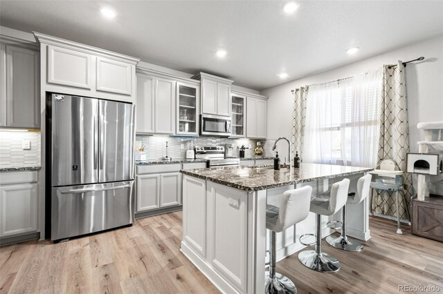 3074 Kestrel St, Brighton, CO 80601 - kitchen with stainless steel appliances, light wood-style floors, dark stone counters, tasteful backsplash, and recessed lighting