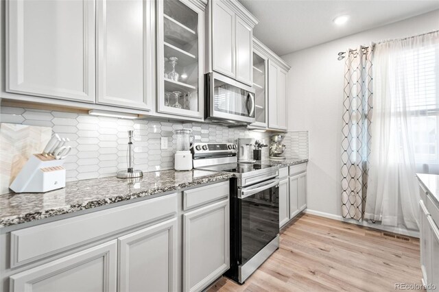3074 Kestrel St, Brighton, CO 80601 - kitchen with stainless steel appliances, glass insert cabinets, light wood-style flooring, light stone counters, and backsplash