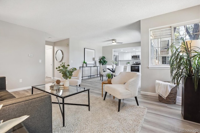 living room with light wood-style floors, baseboards, ceiling fan, and a textured ceiling