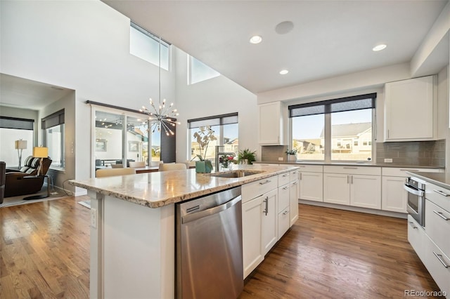 kitchen with white cabinetry, stainless steel appliances, a notable chandelier, an island with sink, and decorative backsplash