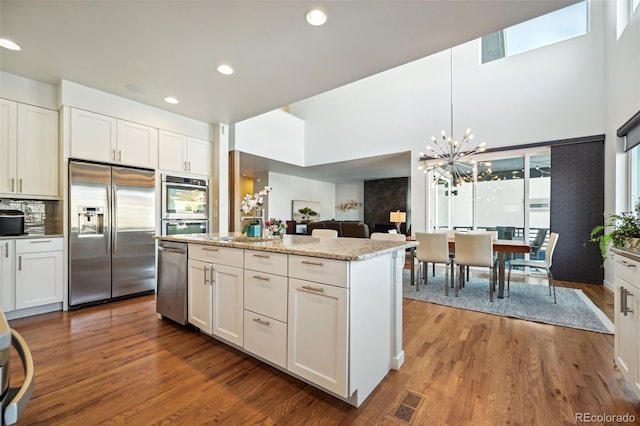 kitchen featuring light stone countertops, stainless steel appliances, white cabinets, a kitchen island, and hanging light fixtures