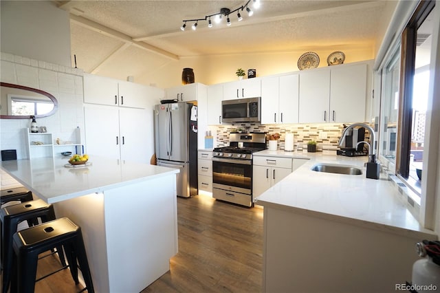 kitchen with lofted ceiling, a kitchen breakfast bar, sink, appliances with stainless steel finishes, and white cabinetry