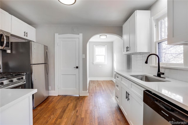 21012103 S Lafayette St, Denver, CO 80210 - kitchen featuring appliances with stainless steel finishes, arched walkways, decorative backsplash, light countertops, and light wood-type flooring