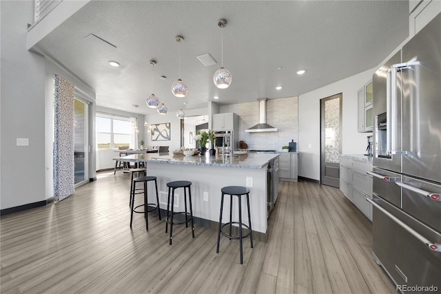 11680 Imboden Rd, Hudson, CO 80642 - kitchen with appliances with stainless steel finishes, wall chimney range hood, a large island, tasteful backsplash, and light wood finished floors