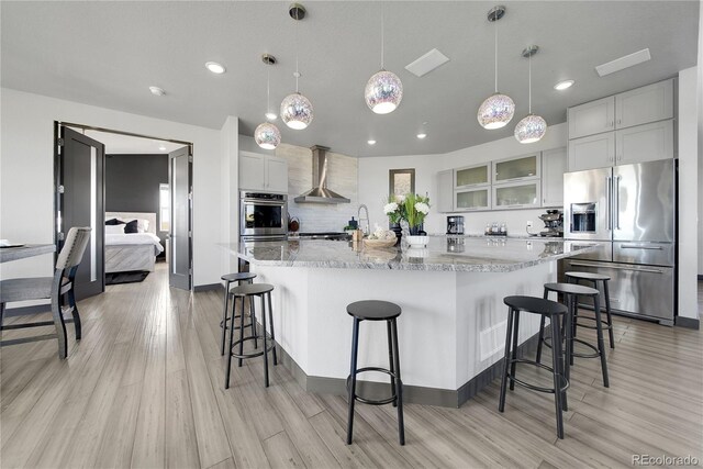 11680 Imboden Rd, Hudson, CO 80642 - kitchen with appliances with stainless steel finishes, wall chimney range hood, light wood-style floors, decorative backsplash, and a breakfast bar area