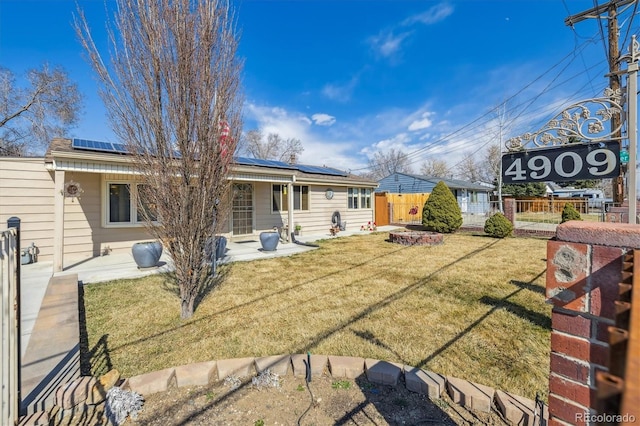 rear view of property featuring a yard, roof mounted solar panels, and fence