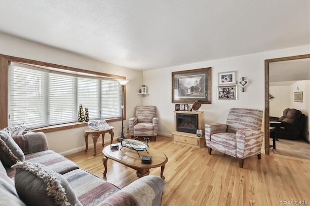 living room with a glass covered fireplace, light wood-type flooring, and baseboards