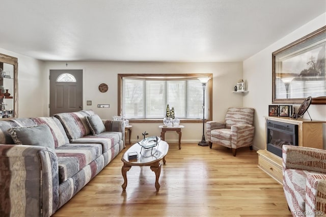 living room featuring light wood-type flooring, baseboards, and a glass covered fireplace