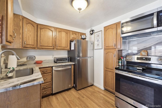 kitchen with brown cabinetry, light wood finished floors, stainless steel appliances, and a sink