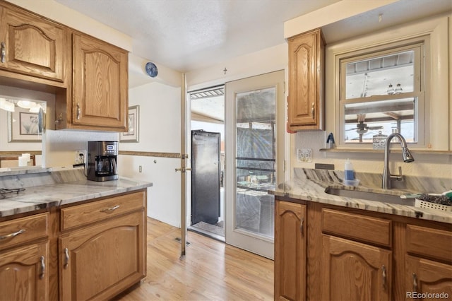 kitchen featuring brown cabinetry, light stone countertops, light wood-type flooring, and a sink