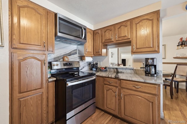 kitchen featuring light wood-type flooring, stainless steel appliances, and brown cabinets