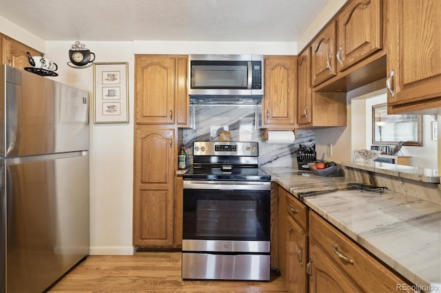 kitchen with light stone counters, stainless steel appliances, brown cabinetry, and light wood finished floors