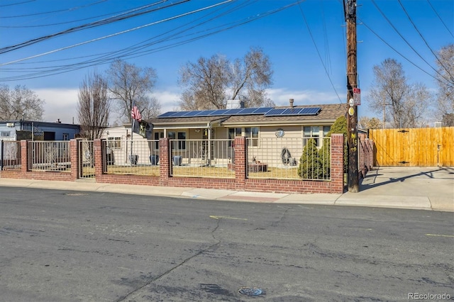 ranch-style house with a fenced front yard, roof mounted solar panels, and a gate