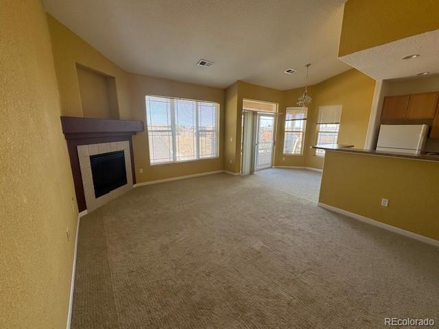 unfurnished living room featuring light colored carpet, a fireplace, visible vents, baseboards, and vaulted ceiling