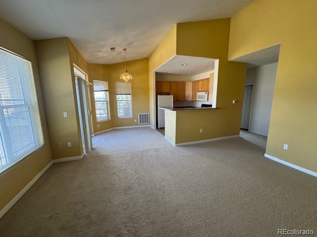 unfurnished living room with lofted ceiling, light colored carpet, visible vents, a chandelier, and baseboards