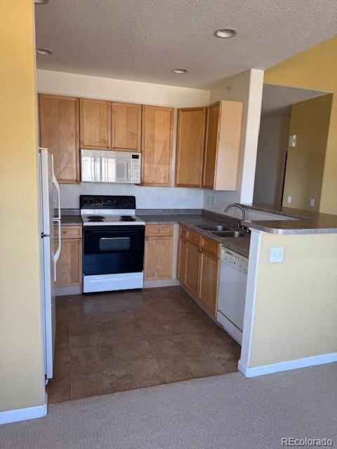 kitchen featuring dark colored carpet, white appliances, a sink, and a textured ceiling