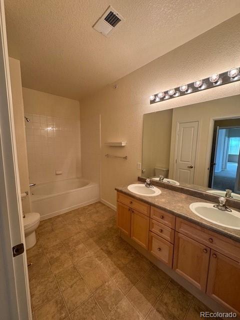 full bath featuring toilet, double vanity, a sink, and visible vents