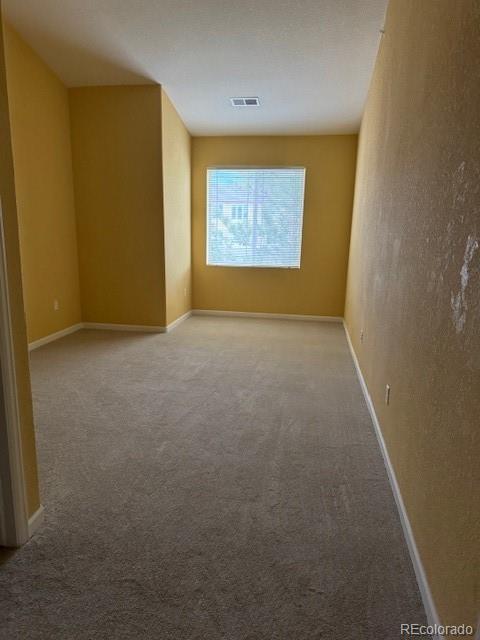 empty room featuring carpet floors, visible vents, and baseboards