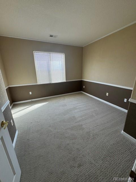 carpeted empty room with ornamental molding, visible vents, a textured ceiling, and baseboards