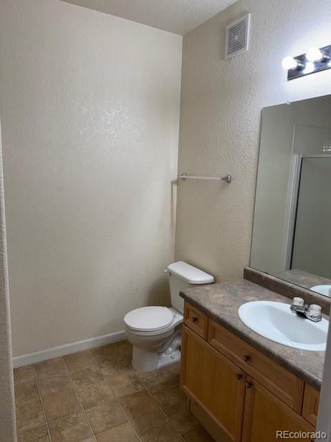 bathroom featuring a textured wall, toilet, vanity, visible vents, and baseboards