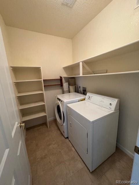 clothes washing area featuring a textured ceiling, laundry area, independent washer and dryer, and baseboards