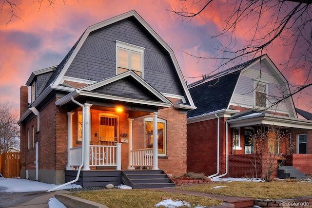 colonial inspired home with covered porch, brick siding, a shingled roof, and a gambrel roof