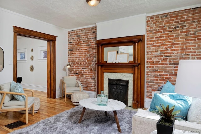 living room with crown molding, brick wall, a textured ceiling, a fireplace, and light wood-style floors