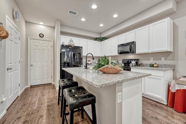 kitchen featuring black appliances, a kitchen island with sink, a kitchen breakfast bar, and white cabinetry